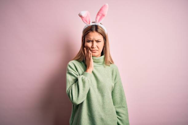 istock Young beautiful woman wearing easter rabbit ears standing over isolated pink background touching mouth with hand with painful expression because of toothache or dental illness on teeth. Dentist 1204798275