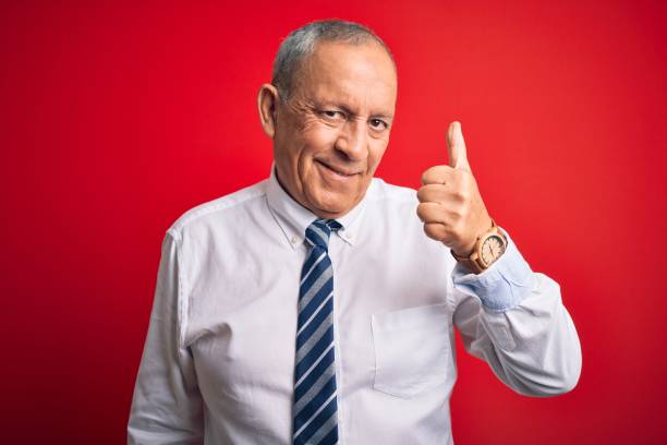 istock Senior handsome businessman wearing elegant tie standing over isolated red background doing happy thumbs up gesture with hand. Approving expression looking at the camera showing success. 1204799149