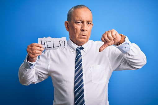 Senior handsome businessman holding paper help message over isolated blue background with angry face, negative sign showing dislike with thumbs down, rejection concept