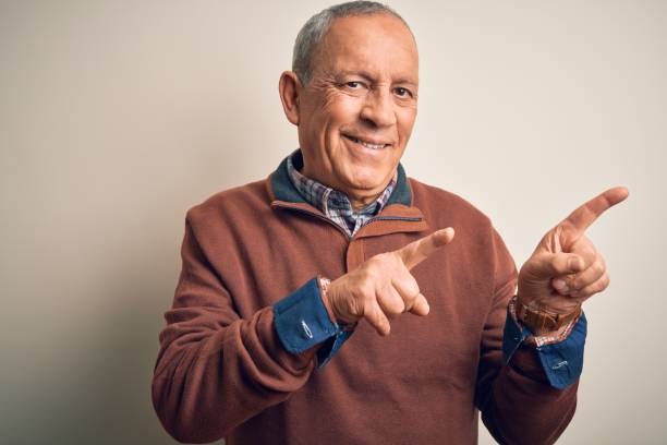 istock Senior handsome man  wearing elegant sweater standing over isolated white background smiling and looking at the camera pointing with two hands and fingers to the side. 1204799191