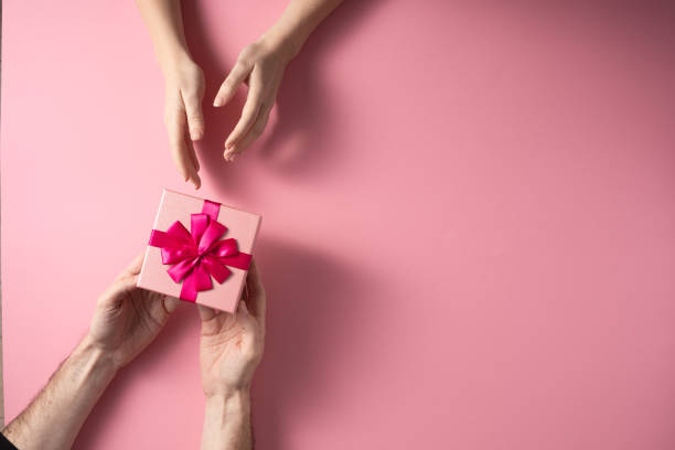istock Valentine's Day celebration concept. A nice gift from a loved one. Box with a bow hands of a man and a woman on a delicate pink background. Copy space. Flat lay. 1204799599