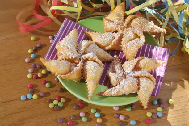 Photo of Traditional carnival pastry, chiacchere or crostoli, bugie, cenci in shape of a toy windmill on table with decorations