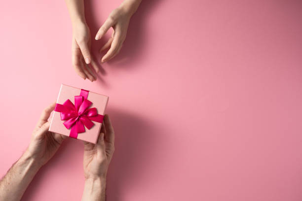 istock Valentine's Day celebration concept. A nice gift from a loved one. Box with a bow hands of a man and a woman on a delicate pink background. Copy space. Flat lay. 1204801348