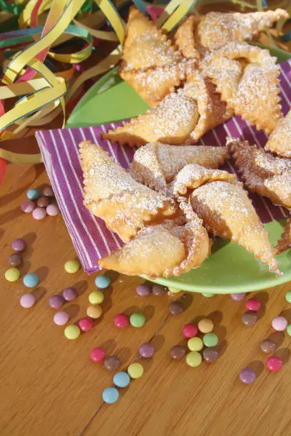 Photo of Traditional carnival pastry, chiacchere or crostoli, bugie, cenci in shape of a toy windmill on table with decorations