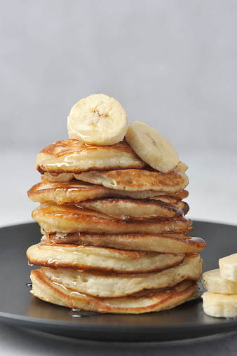 A pile of fritters on a black plate.  On the top pancake, slices of banana.  Pancakes are watered with honey.  The vertical orientation of the frame. Close-up.