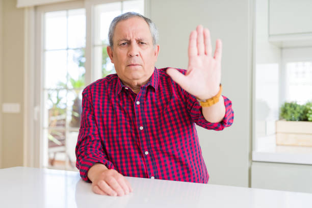 istock Handsome senior man at home doing stop sing with palm of the hand. Warning expression with negative and serious gesture on the face. 1204803729