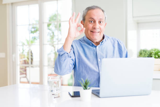 istock Handsome senior man using computer laptop working on internet doing ok sign with fingers, excellent symbol 1204803936