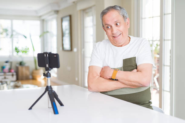 istock Handsome senior man doing video conference talking to the smartphone camera happy face smiling with crossed arms looking at the camera. Positive person. 1204805340