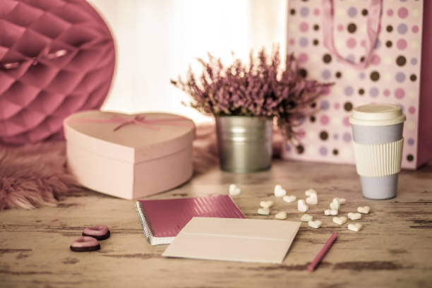 Flat lay of romantic, pink pastel arrangement of a love note, heart shaped gift box and candy, some flowers and a disposable cup of coffee waiting for the loved one on Valentine's day.