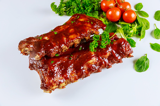 Barbecued sticky spare ribs on a white isolated background with tomato and herbs.