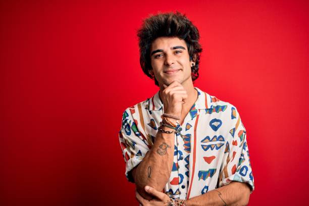 istock Young handsome man on vacation wearing summer shirt over isolated red background looking confident at the camera smiling with crossed arms and hand raised on chin. Thinking positive. 1204810367