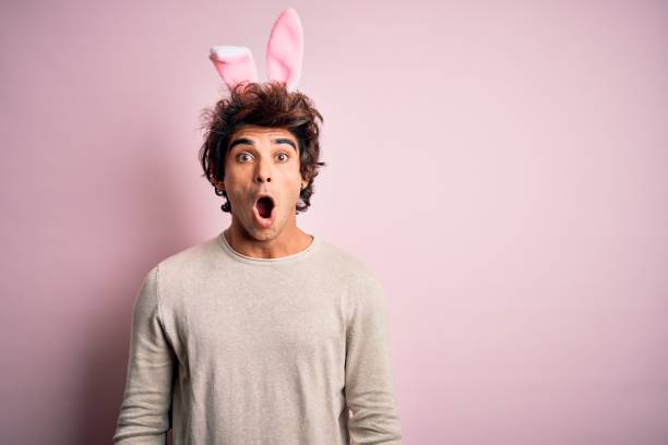 istock Young handsome man holding easter rabbit ears standing over isolated pink background afraid and shocked with surprise expression, fear and excited face. 1204811285