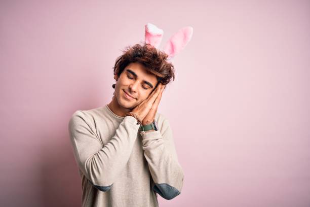 istock Young handsome man holding easter rabbit ears standing over isolated pink background sleeping tired dreaming and posing with hands together while smiling with closed eyes. 1204811366