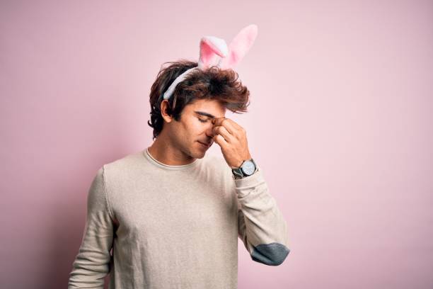 istock Young handsome man holding easter rabbit ears standing over isolated pink background tired rubbing nose and eyes feeling fatigue and headache. Stress and frustration concept. 1204811369