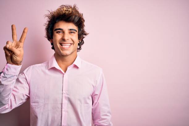 istock Young handsome man wearing king crown standing over isolated pink background smiling with happy face winking at the camera doing victory sign. Number two. 1204811431
