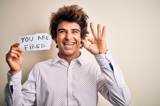 Young handsome man holding paper with message standing over isolated white background doing ok sign with fingers, excellent symbol