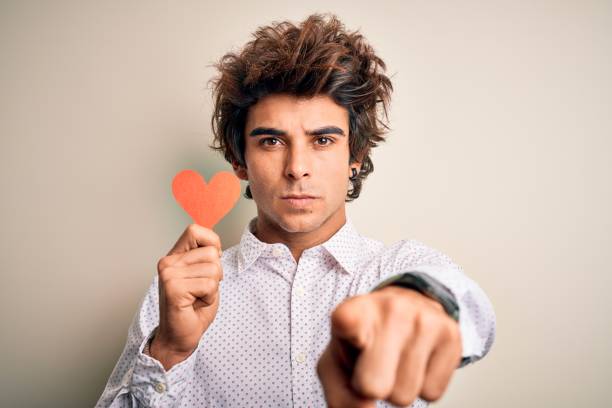 istock Young handsome man holding paper heart standing over isolated white background pointing with finger to the camera and to you, hand sign, positive and confident gesture from the front 1204811468