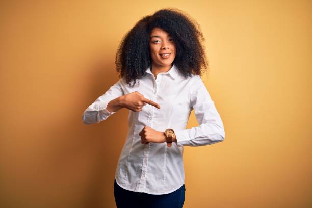 giovane bella donna elegante afroamericana con i capelli afro in piedi su sfondo giallo in fretta indicando il tempo di guardare il tempo, impazienza, sconvolto e arrabbiato per il ritardo della scadenza - checking the time women impatient wristwatch foto e immagini stock