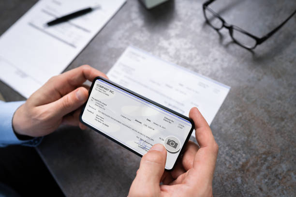Man Taking Photo Of Cheque To Make Remote Deposit Man Taking Photo Of Cheque To Make Remote Deposit In Bank bank deposit slip stock pictures, royalty-free photos & images