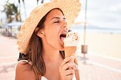 Young beautiful woman eating ice cream cone by the beach on a sunny day of summer on holidays