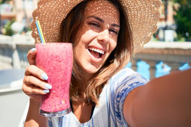 donna beutiful seduta al bar della piscina bevendo frullato sano e scattando selfie con lo smartphone - blueberry smoothie milk shake drink foto e immagini stock