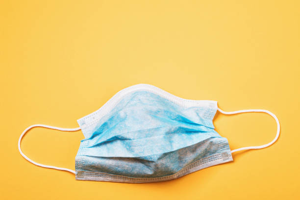 istock Blue disposable medical mask on a yellow background with copy space, top view 1204827242