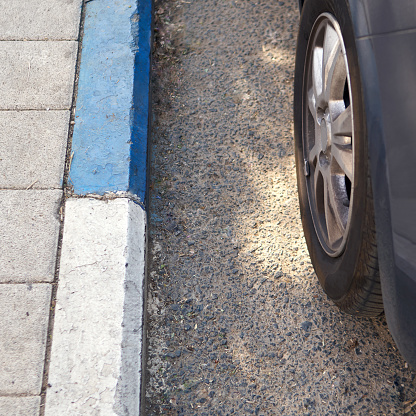 Wheel of a car stands near a road curbstone painted in blue and white colors which indicate a paid Parking in Israel.