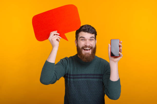 istock Happy handsome man holding red speech bubble and showing smartphone screen, best offer 1204840933