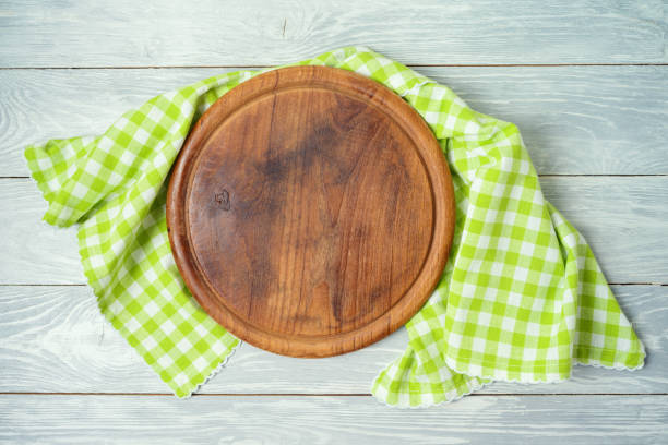 istock Round pizza board with green checked tablecloth on rustic wooden table .Kitchen, cooking or baking mock up background for design. 1204841066