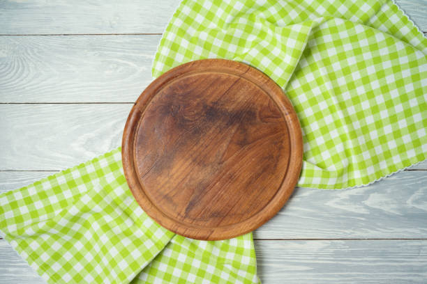 istock Round pizza board with green checked tablecloth on rustic wooden table .Kitchen, cooking or baking mock up background for design. 1204841071
