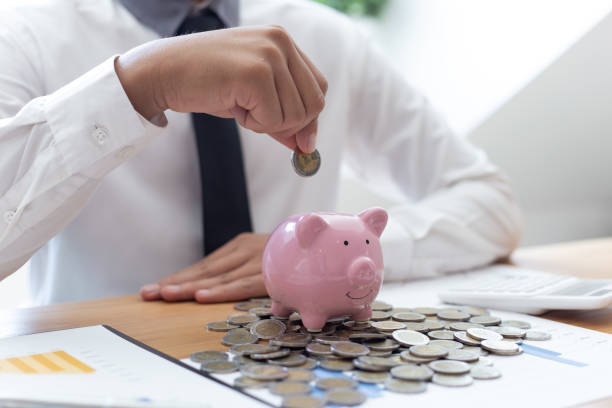 istock Midsection Of Man Inserting Coin In Piggy Bank On Table 1204845497