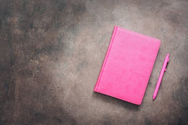 istock Pink notebook and pen on a dark vintage background, toned. Female workspace. Top view, flat lay, copy space. 1204848045