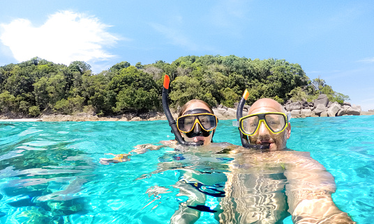 Young couple taking selfie in tropical scenario with waterproof camera - Boat trip snorkeling excursion at Similan islands - Youth lifestyle and travel concept around world - Bright vivid filter