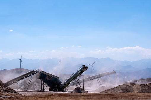 Excavator digs against and wind turbine farm.