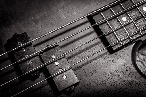 Bass guitar with four strings in black and white closeup. Detail of popular rock musical instrument. Close view of wooden textured electric bass. Vintage style photo of bass guitar pickups and neck.