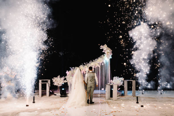 istock Wedding Fire show and fire heart at night on black background. Burning heart with fireworks. Brides holding hands and looking at fireworks and fire show. 1204862792