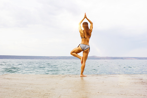 Shot of an athletic young woman practicing yoga on the beach, before swim