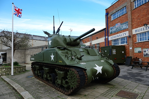 Portland Dorset. England. Exterior of the D-Day invasion museum showing Sherman tank and signage. Flags flying. Red brick building. tank has machines guns on turret.