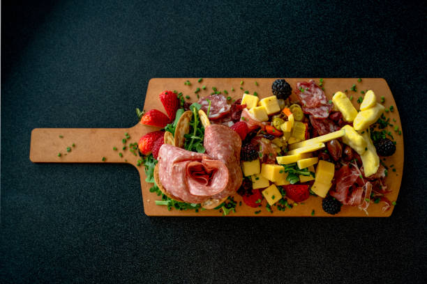 un piatto di salumi organizzato con una varietà di salumi, formaggi e frutta - wine cheese food salami foto e immagini stock
