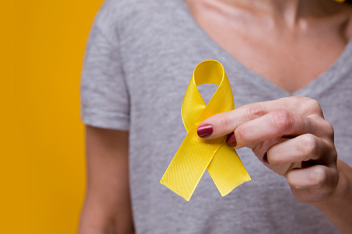 Young female holding yellow gold ribbon awareness symbol for endometriosis, suicide prevention, sarcoma bone cancer, bladder cancer, liver cancer and childhood cancer concept. Health care. Close up.