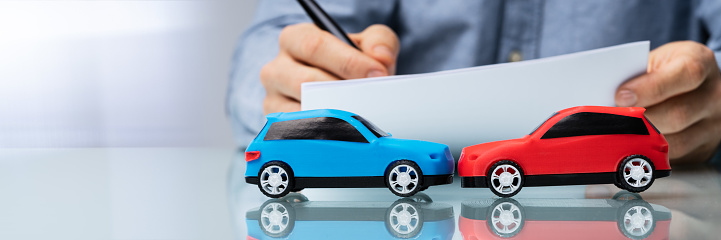 Close-up Of Red And Blue Car In Front Of Businessman Writing On Paper