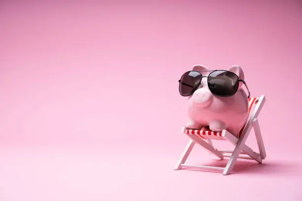 Pink Piggy Bank With Sunglasses On The Small Deck Chair On Pink Background