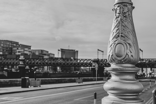The base of an ornate street lamp with railway bridge in the distance.  Dublin, Ireland.