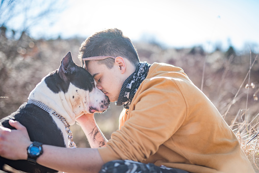 Young Man Hugging and Kissing His Dog in Nature .