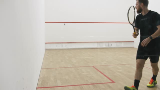 Young athletic man and woman play squash together in the squash court, slow motion