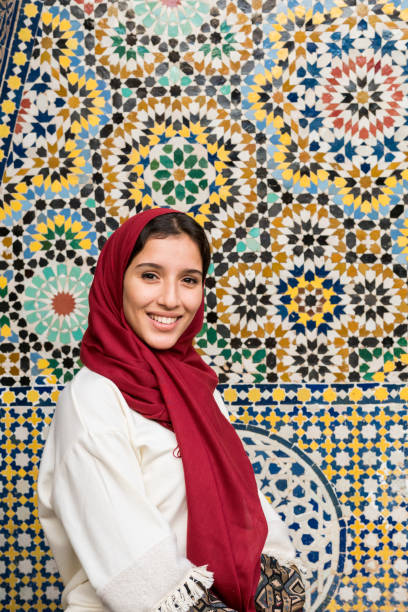 Portrait of muslim woman smiling in traditional clothing with red headscarf on her head Portrait of young muslim woman smiling in traditional clothing with red hijab in front of traditional arabesque decorated wall moroccan woman stock pictures, royalty-free photos & images