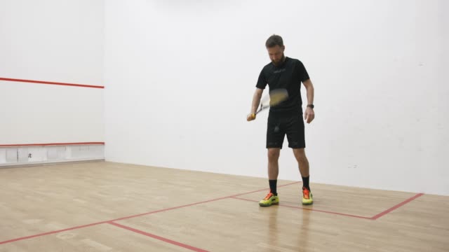 A portrait of a young bearded man serving the ball in the squash cort