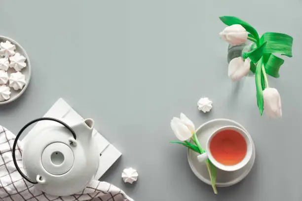 Geometric panoramic flat lay with hands. Cup of black tea, tea pot, sweets and white tulips on grey with copy-space. Valentine day, Mother's day, international women day March 8. Trendy border.