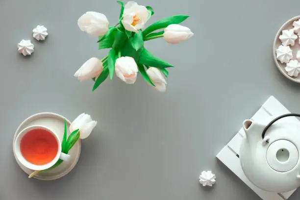 Mother;s day tea table set. Trendy modern flat lay, top view. Tea pot, sweets and white tulips on light silver grey paper.
