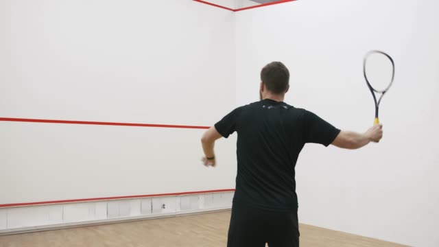A portrait of a young bearded man practicing to play squash, slow motion